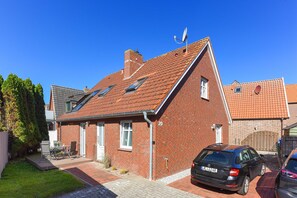 A red-brick house with a sloped roof, a satellite dish, and a car parked in the driveway.