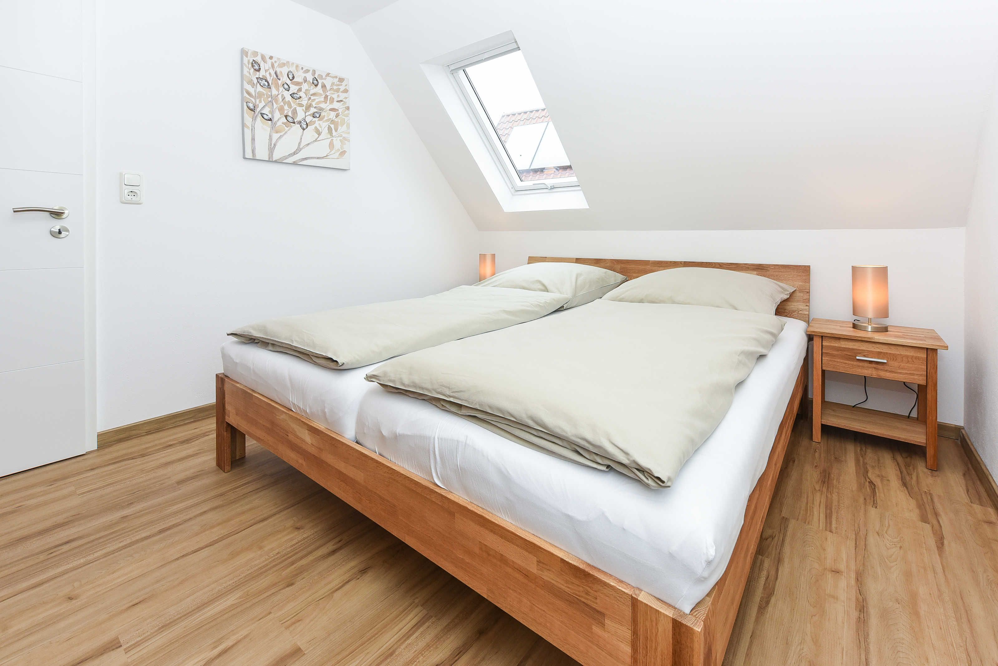 Ein Schlafzimmer mit einem hölzernen Bett, einem Oberlicht, einem Nachttisch mit Lampe und einer Tür.