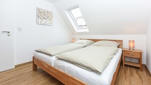 Quarto com cama de madeira, claraboia, mesa de cabeceira com luminária e porta.