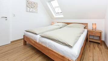 Ein Schlafzimmer mit einem hölzernen Bett, einem Oberlicht, einem Nachttisch mit Lampe und einer Tür.