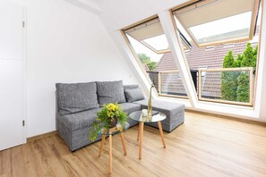 Un dormitorio tipo loft moderno con techo inclinado, un sofá gris, una mesa de centro de vidrio y vistas a una zona residencial.