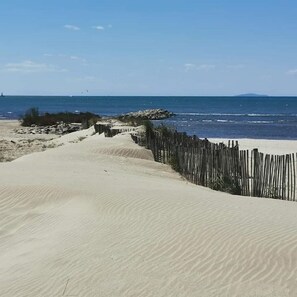 Ein sandiger Strand mit einer Holzzaun und einem Felsen im Hintergrund.