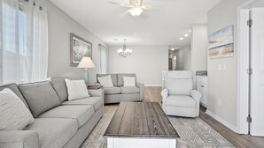 Un salon moderne avec un canapé d’angle gris, un fauteuil blanc et une table basse en bois.