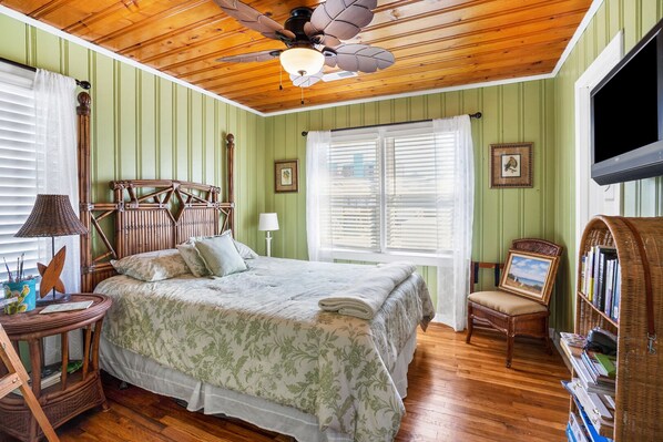 A bedroom with a wooden ceiling, a bed with a floral bedspread, a wicker chair, a bookshelf, and a ceiling fan. - Amazing channel views, close to beach w/mother-in-law suite in North Myrtle Beach (North Myrtle Beach)