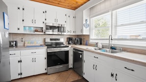 Een moderne keuken met witte kasten, roestvrijstalen apparatuur en een raam met jaloezieën.