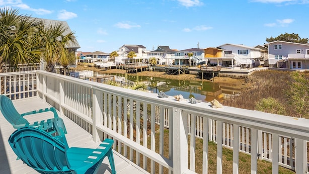 Een terras met turquoise stoelen met uitzicht op een waterpartij en huizen.