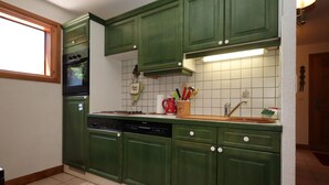 Une cuisine avec des meubles de couleur verte, un lave-vaisselle, une cuisinière et une fenêtre.