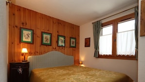 Une chambre avec des murs recouverts de panneaux de bois, un lit doté d’une tête de lit à carreaux verts, une table de chevet avec une lampe et une fenêtre avec des rideaux.