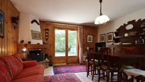 Un salon chaleureux avec une cheminée, des murs en bois, un canapé rouge et un coin repas comprenant une table et des chaises.