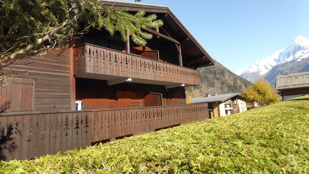 Un chalet en bois doté d’un balcon, entouré d’une pelouse et avec des montagnes en toile de fond.