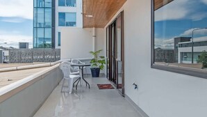 A balcony with a table and chairs, a potted plant, and a view of a modern building.