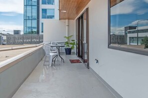 A balcony with a table and chairs, a potted plant, and a view of a modern building.