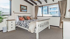 A bedroom with a bed, bedside tables, a lamp, a window with curtains, and a painting on the wall.