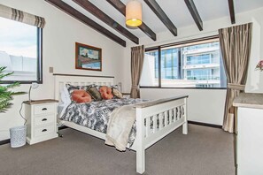 A bedroom with a bed, bedside tables, a lamp, a window with curtains, and a painting on the wall.