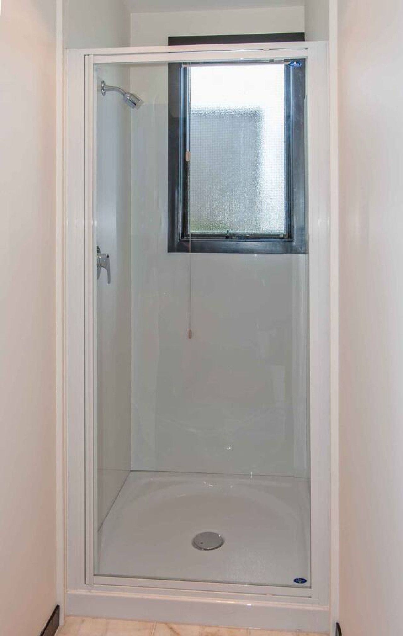 A glass-enclosed shower stall with a small window at the top.