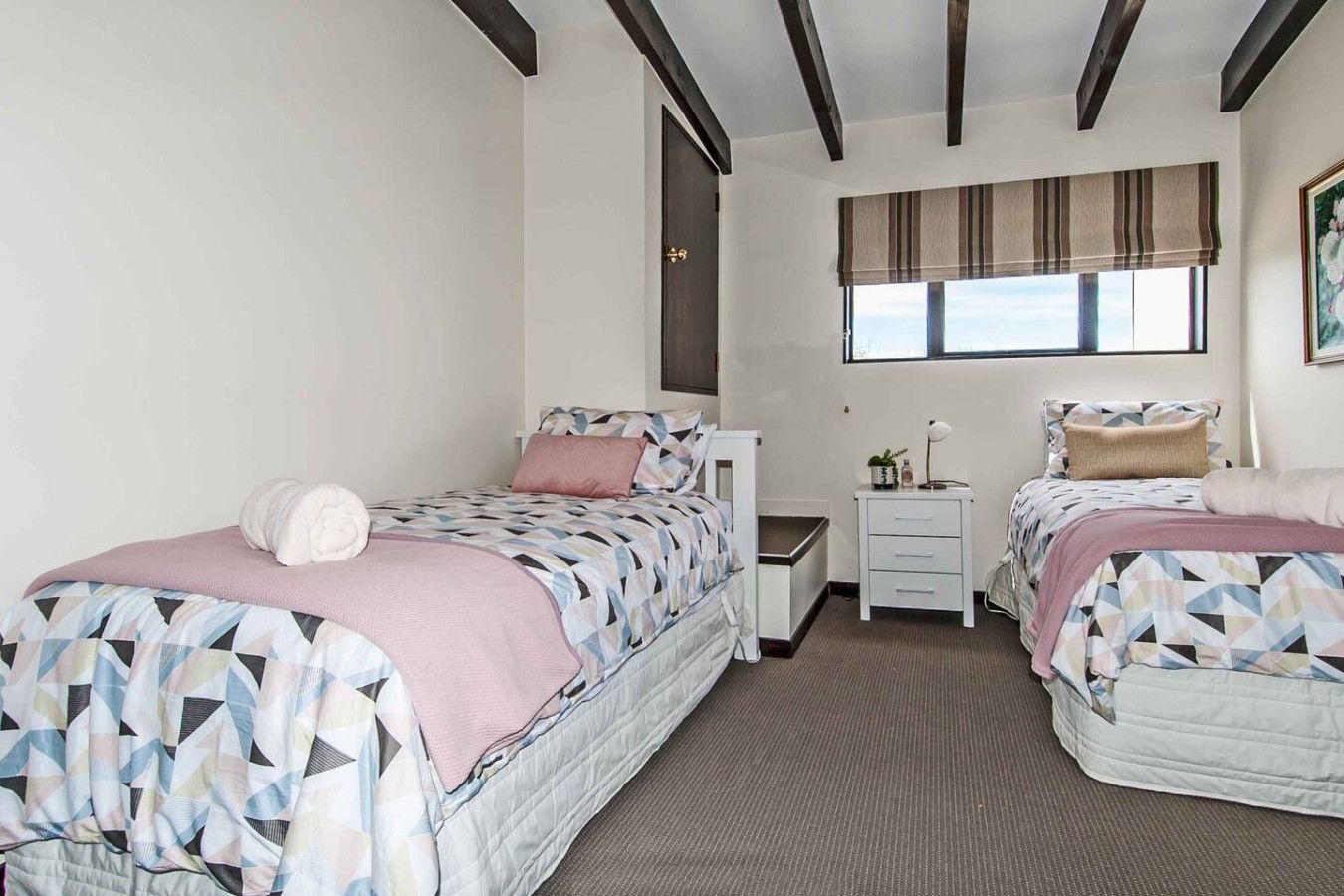 A twin bedroom with two beds, a nightstand, a window with curtains, and a painting on the wall.