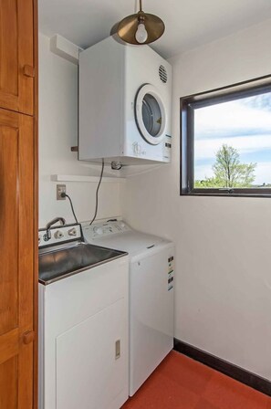 Ein Waschraum mit Waschmaschine, Trockner und einem Fenster mit Blick auf Bäume.