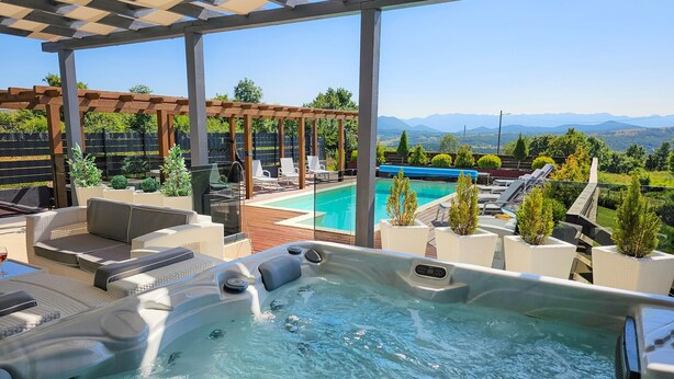 Un jacuzzi con piscina, mobiliario de exterior y vistas a montañas.