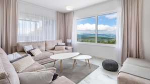 Una sala de estar moderna con un sofá, dos mesas redondas de centro y vistas a un paisaje montañoso a través de un ventanal grande.