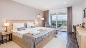 Una habitación de hotel moderna con una cama grande, dos mesitas de noche con lámparas, un escritorio con una silla y un balcón con vistas.