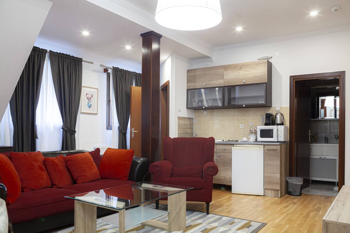 Un espacio habitable compacto con sofá, sillón, una mesa de centro de vidrio, kitchenette y comedor.