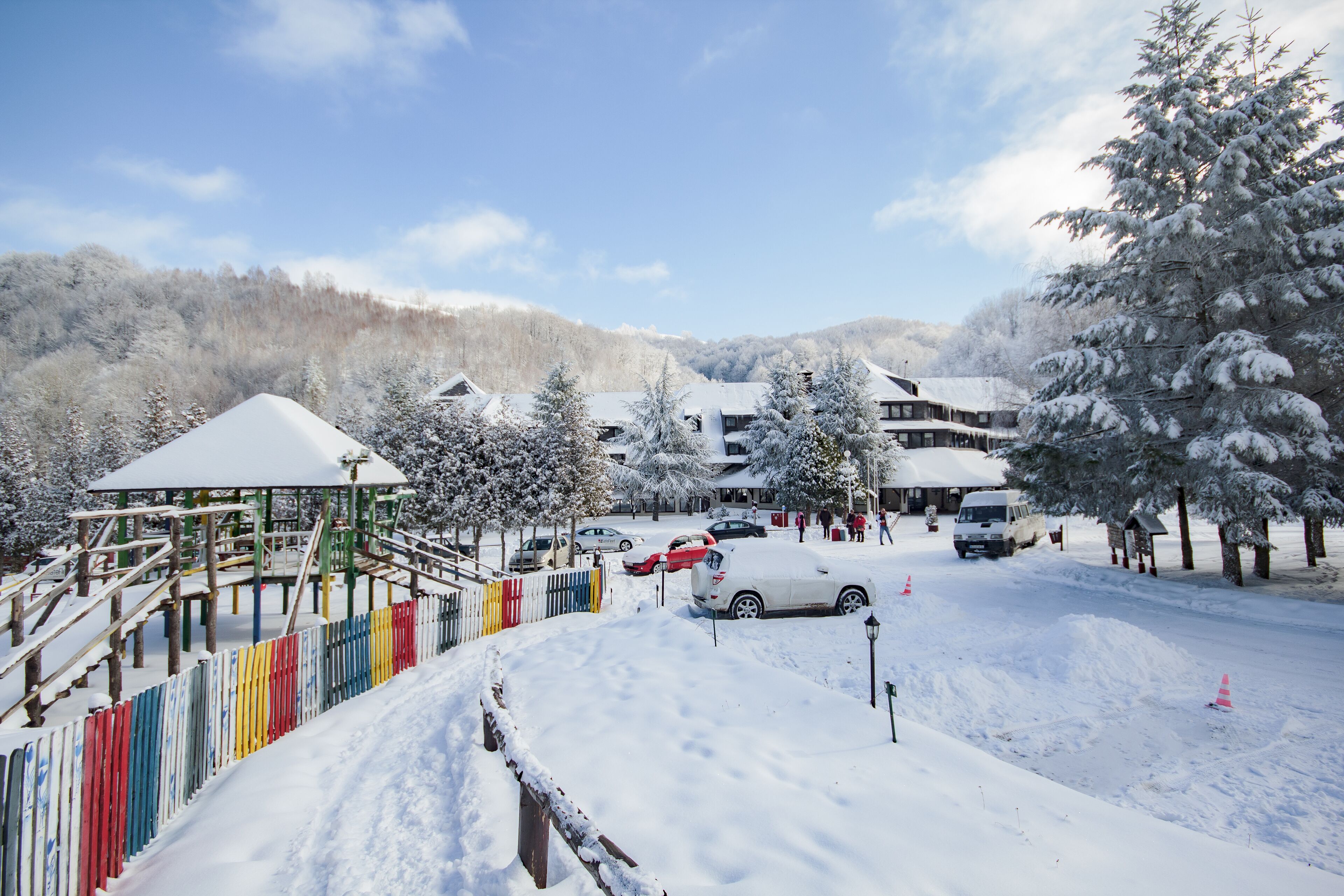 A snowy landscape with a playground, a covered area, and a building with a snow-covered roof.