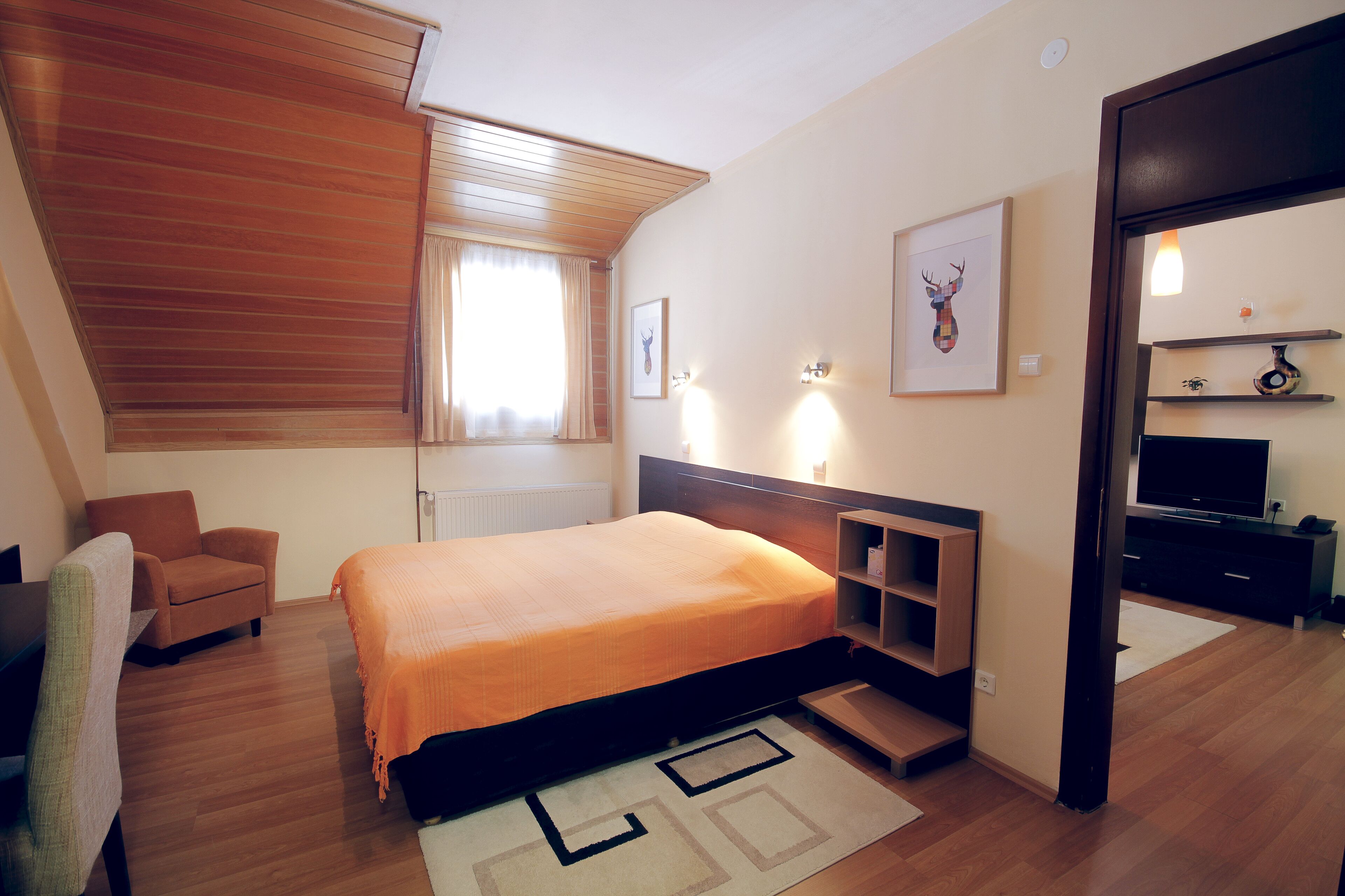 Un dormitorio con cama, una silla, un escritorio, un televisor y una estantería con adornos.