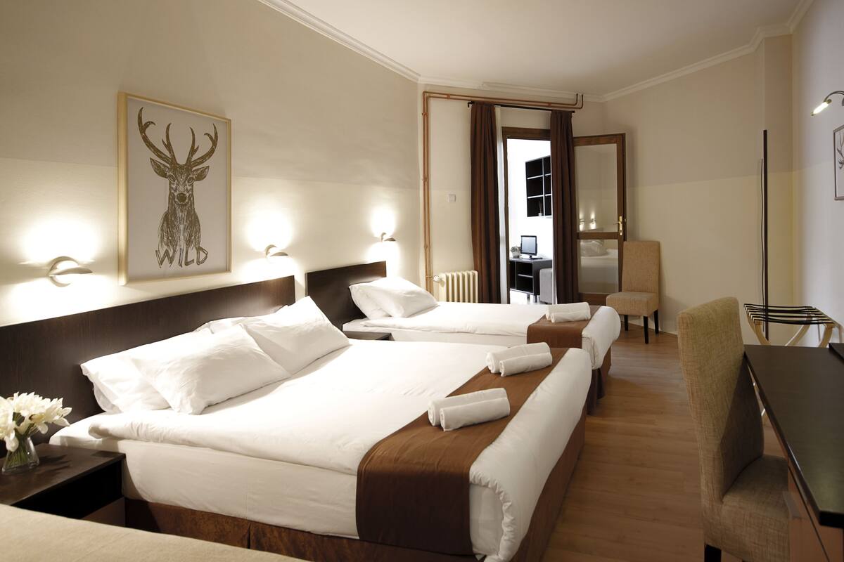Una habitación de hotel con dos camas, un escritorio, una silla, un espejo y un cuadro en la pared.
