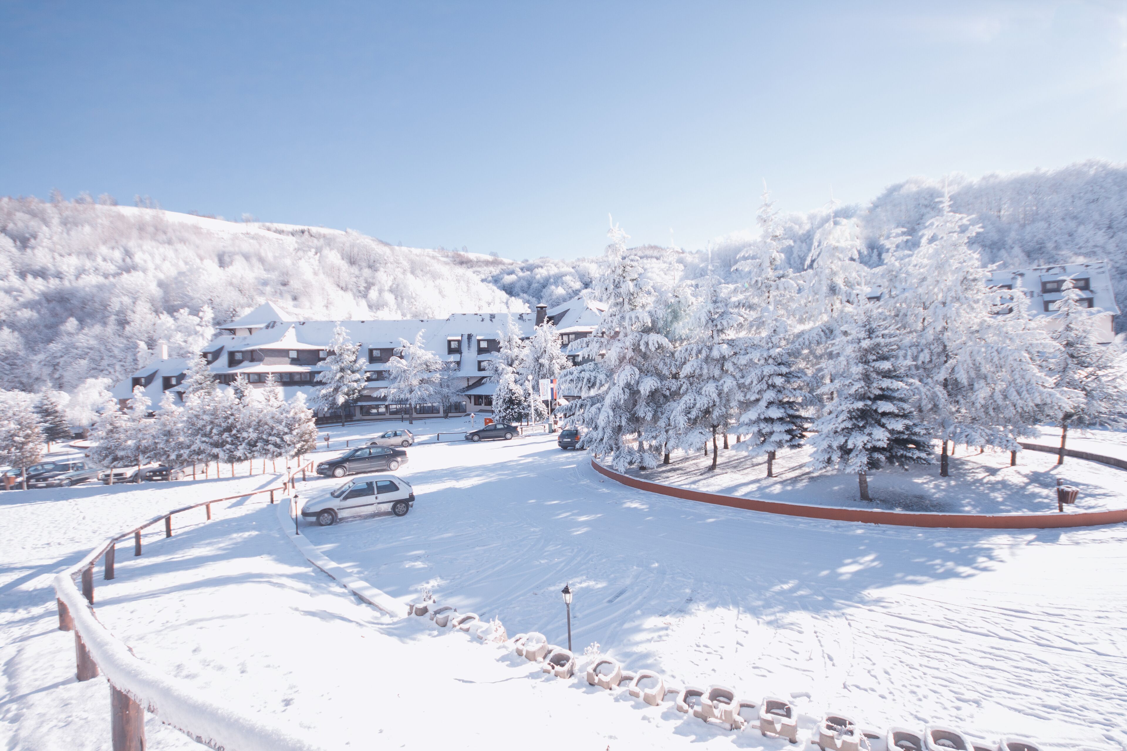 Uma área de estacionamento coberta de neve, com carros, um caminho sinuoso e edifícios ao fundo.