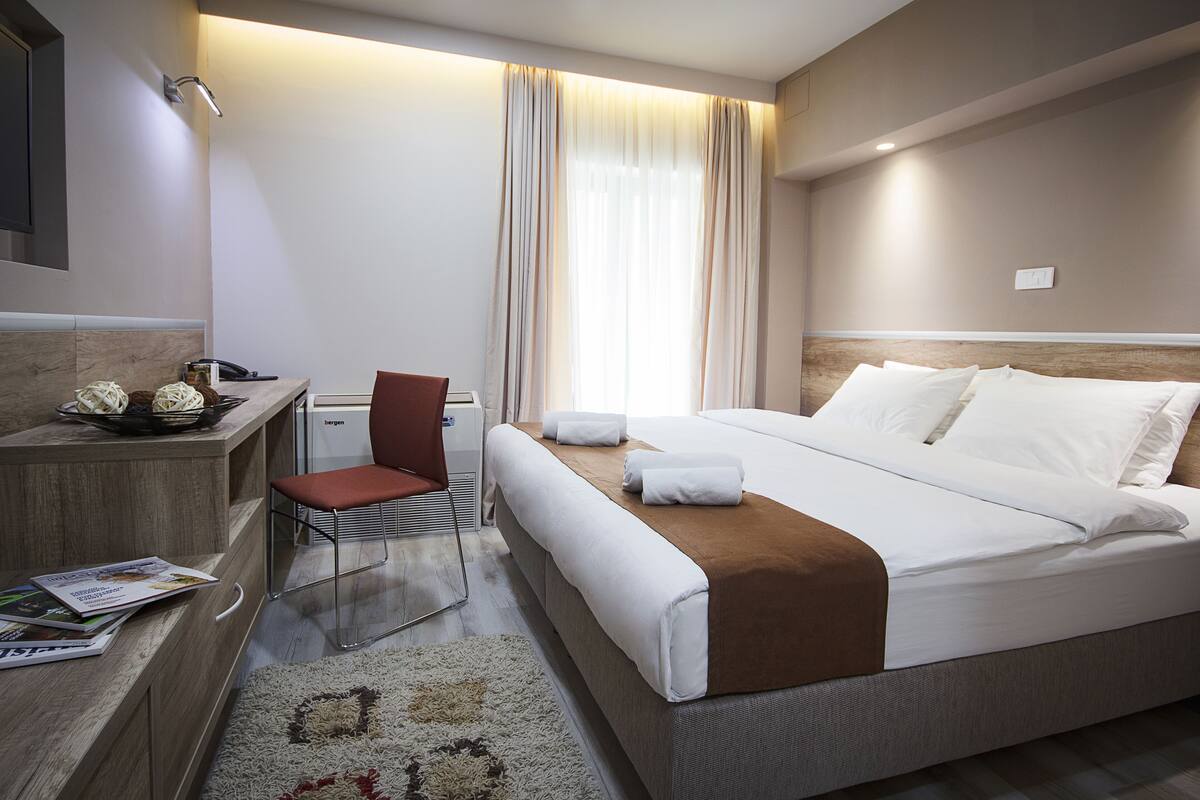 Una habitación de hotel con una cama, un escritorio, una silla y una ventana con cortinas.