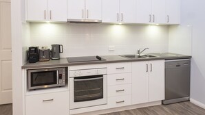 A modern kitchen with white cabinets, a microwave, an oven, a coffee maker, a dishwasher, and a sink. - Villa 17  Beaches Bush Wineries and more (Dunsborough)