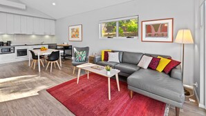 A modern living room with a grey sofa, red rug, and a dining area with a table and chairs. - Villa 17  Beaches Bush Wineries and more (Dunsborough)