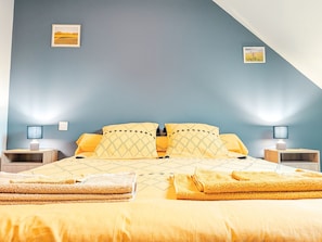 Ein Schlafzimmer mit einem Bett, zwei Nachttischen, zwei Lampen, zwei Kissen, zwei Decken, zwei Handtüchern und zwei gerahmten Bildern an der Wand.