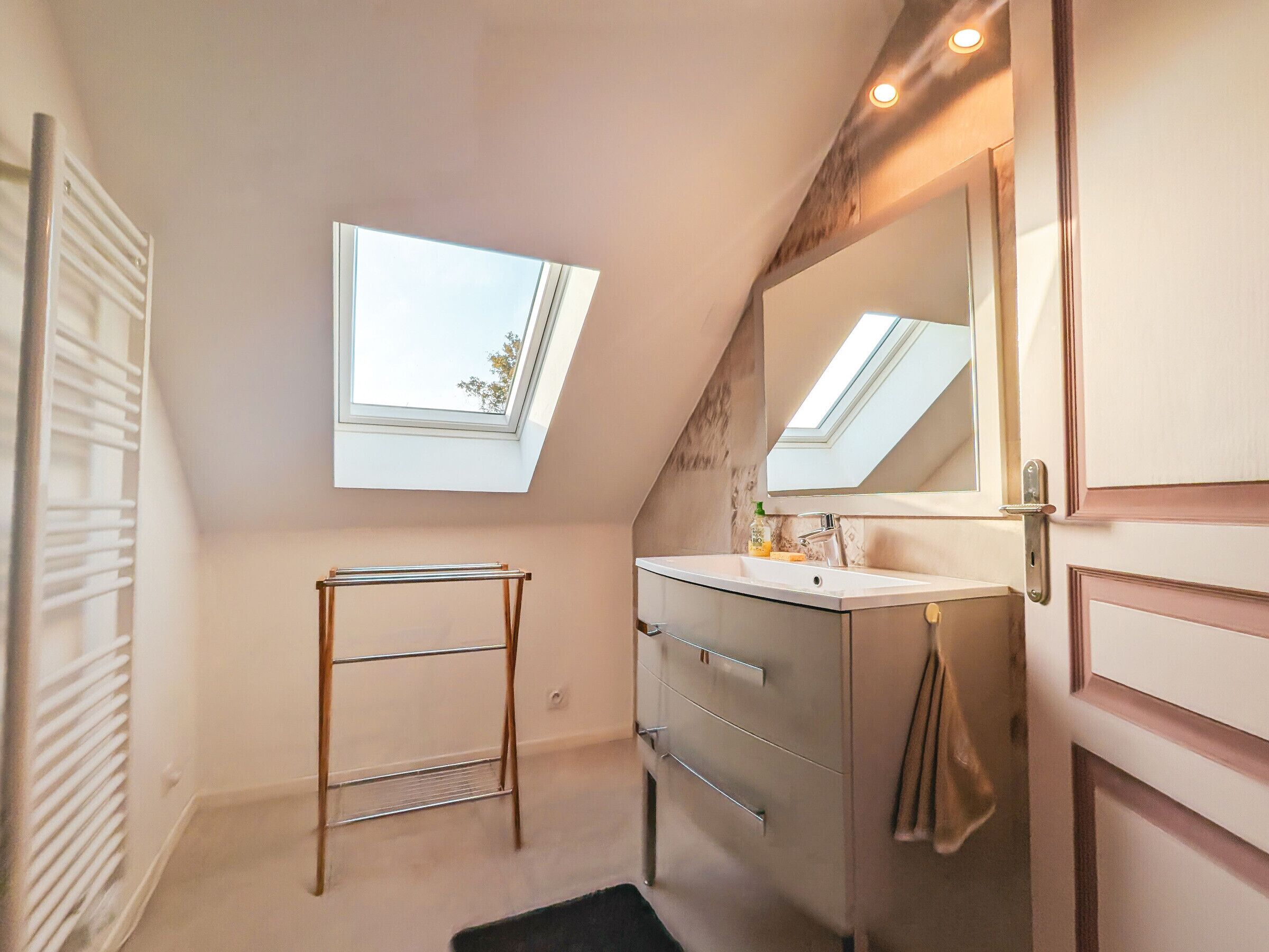 Une salle de bain moderne dotée d’une lucarne, d’un meuble-lavabo avec miroir et d’un porte-serviettes.