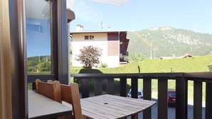 Un balcon avec une table et des chaises en bois, donnant sur un quartier résidentiel avec une montagne en arrière-plan.