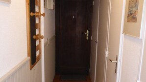 A narrow hallway with wooden flooring, a dark door at the end, and a white wall with a small picture frame.