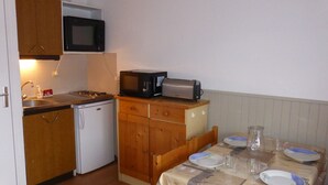 A compact kitchen with a microwave, toaster, and small refrigerator. There is a dining table set with plates and glasses.