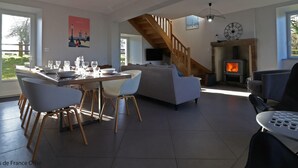 Ein geräumiger Wohnbereich mit Esstisch für vier Personen, Kamin und einer Treppe, die in eine obere Ebene führt.