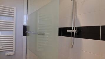 Un baño moderno con cabina de ducha de vidrio, toallero blanco y paredes de azulejos blanco y negro.
