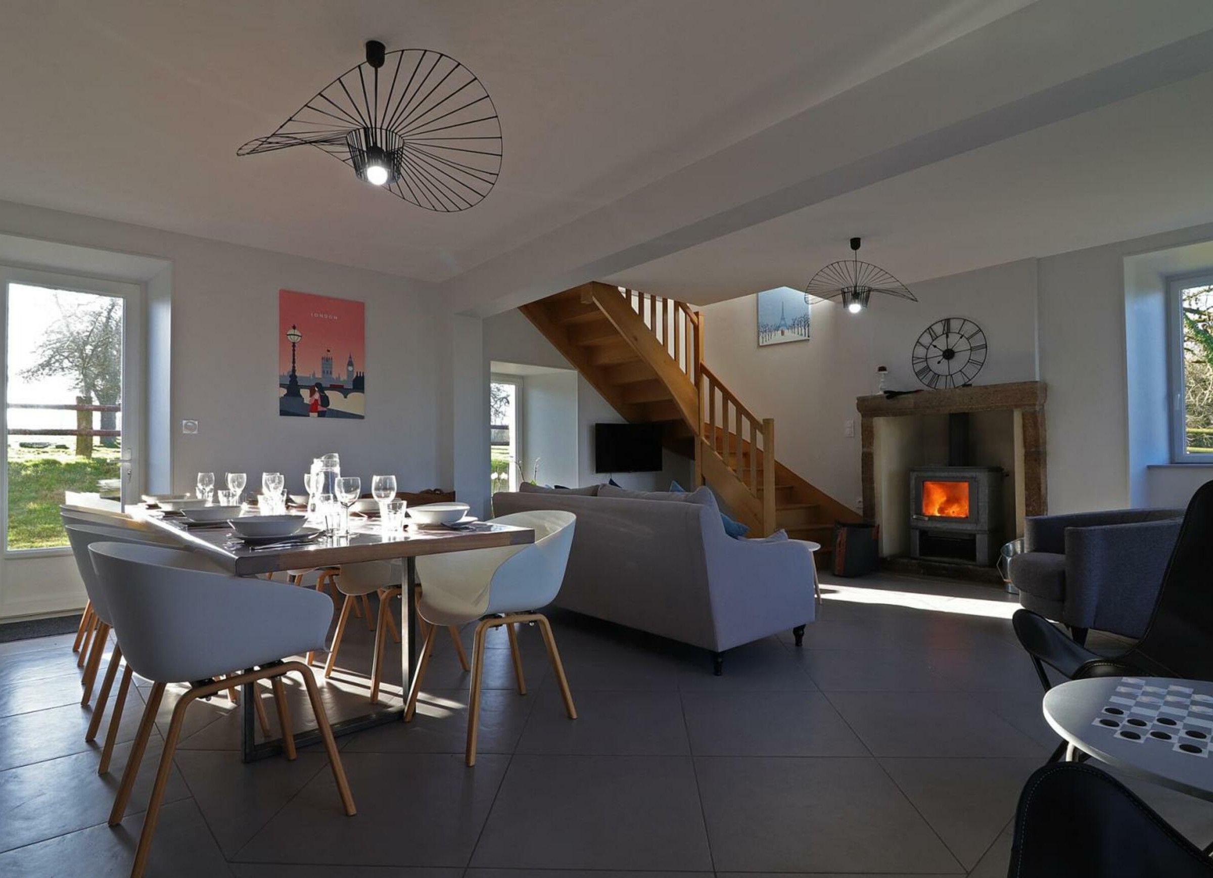 Een ruime woonkamer met een eettafel voor vier personen, een open haard en een trap naar een hoger gelegen verdieping.