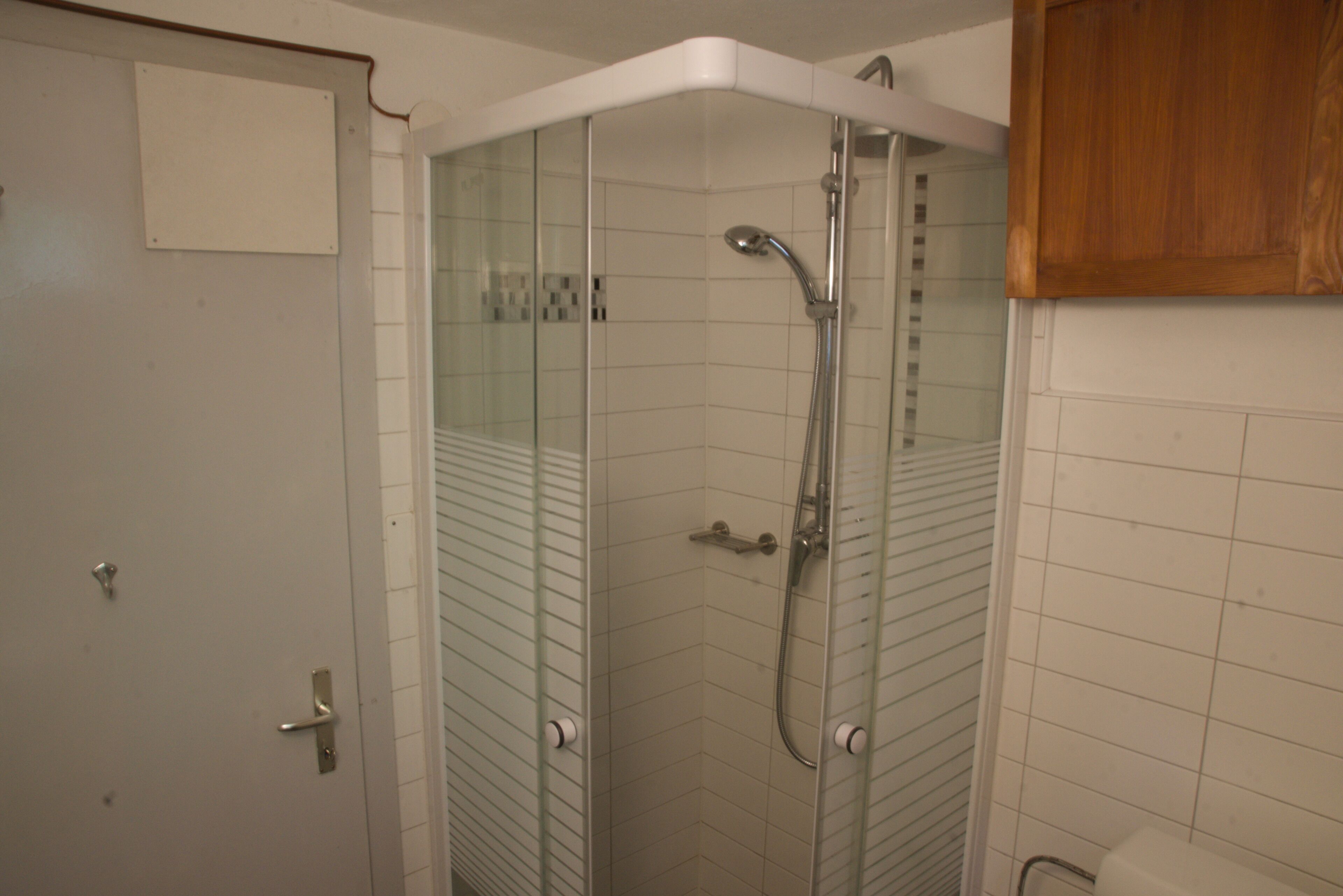 Une douche fermée par des parois en verre, dotée d’un pommeau de douche à main et d’un robinet mural.