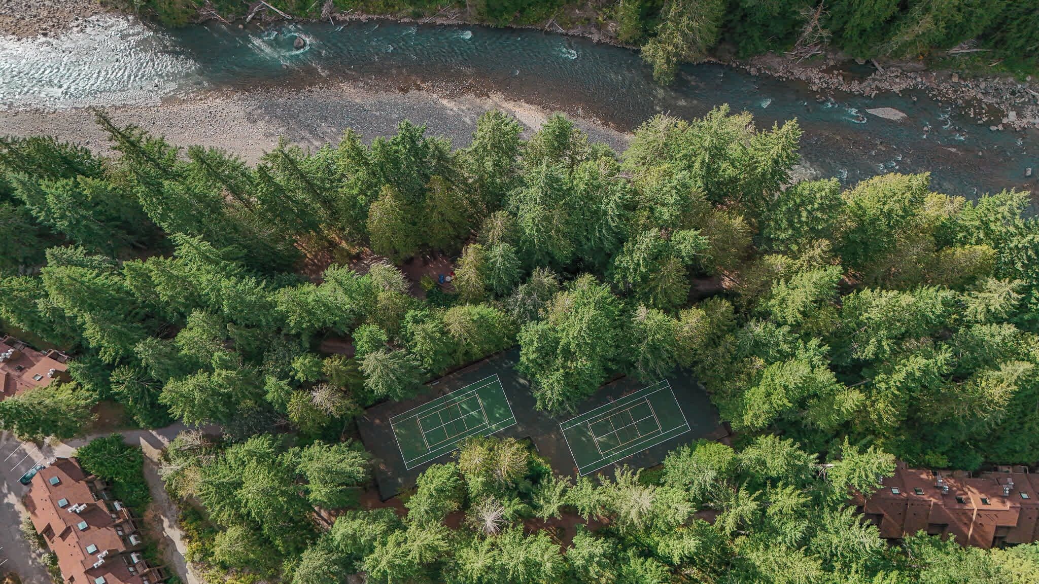 Vue aérienne d’un quartier résidentiel caractérisé par une végétation dense, un court de tennis et une rivière.