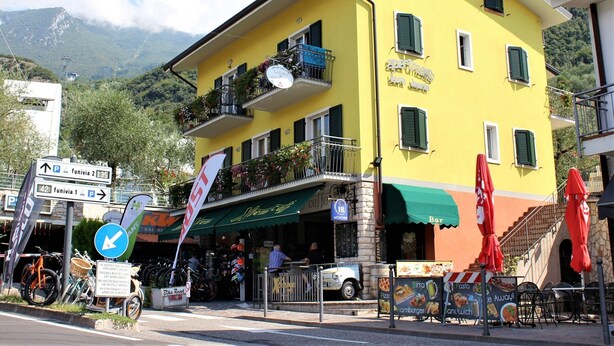 Un edificio amarillo con balcones, una cafetería y un letrero de alquiler de bicicletas.