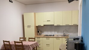Una cocina compacta con una mesa de comedor, sillas, una cafetera y un televisor montado en la pared.