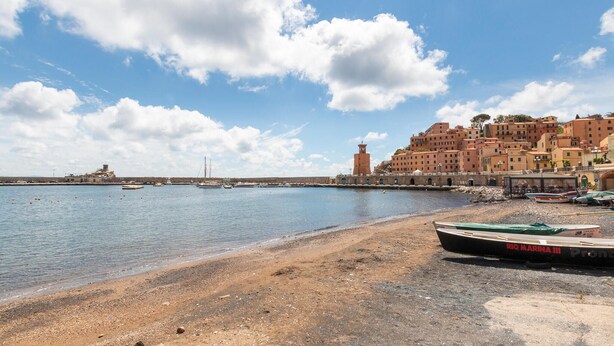 A coastal town with a lighthouse, boats, and a beach.