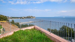 A coastal view with a metal railing, a beach, and buildings in the distance.