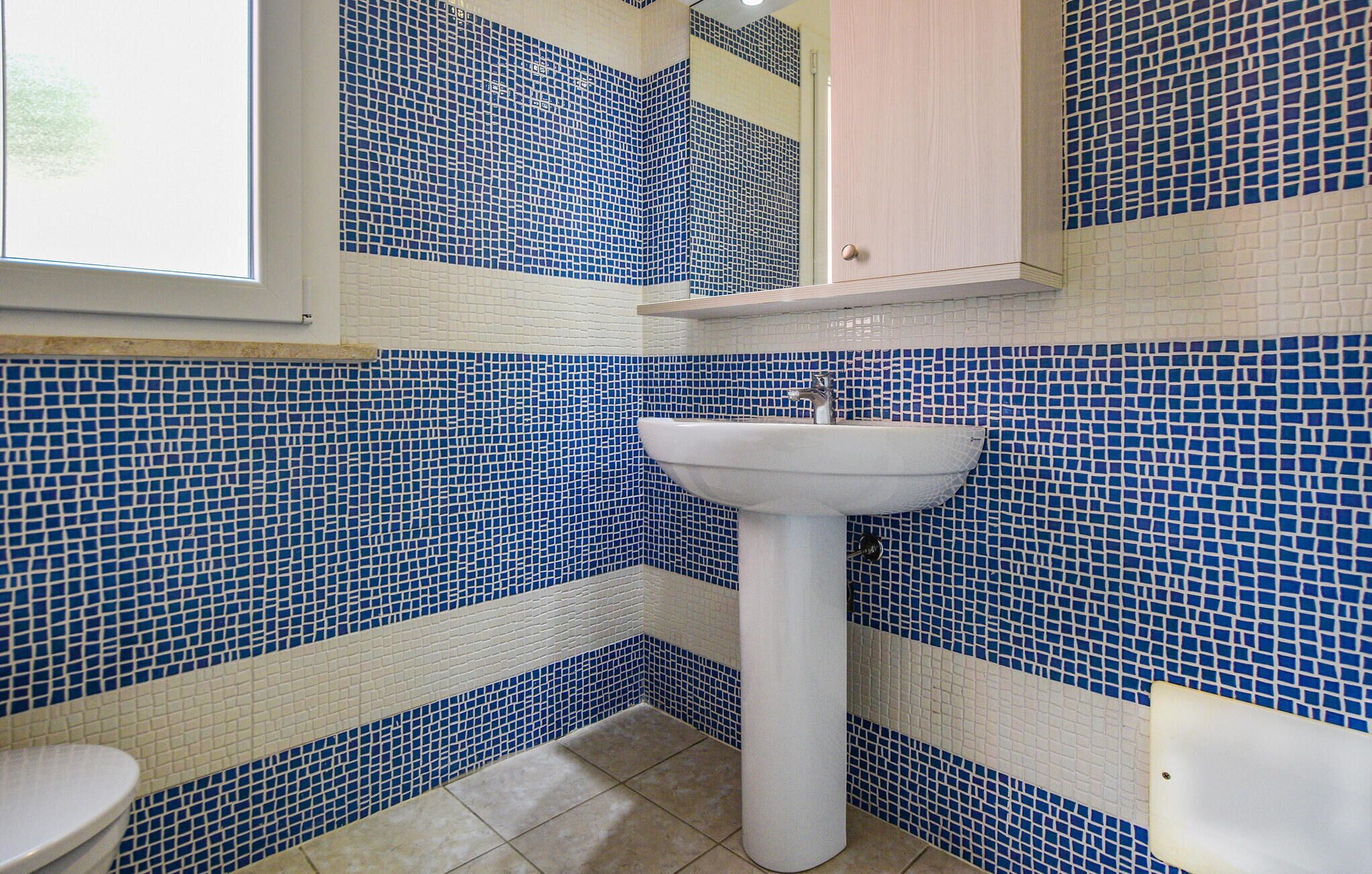 Une salle de bain avec des murs recouverts de mosaïques bleues et blanches, un lavabo blanc et un meuble en bois au-dessus du lavabo.