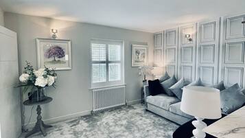 A living room with a grey carpet, a grey sofa with cushions, a coffee table, a side table with a vase of flowers, and framed pictures on the wall.