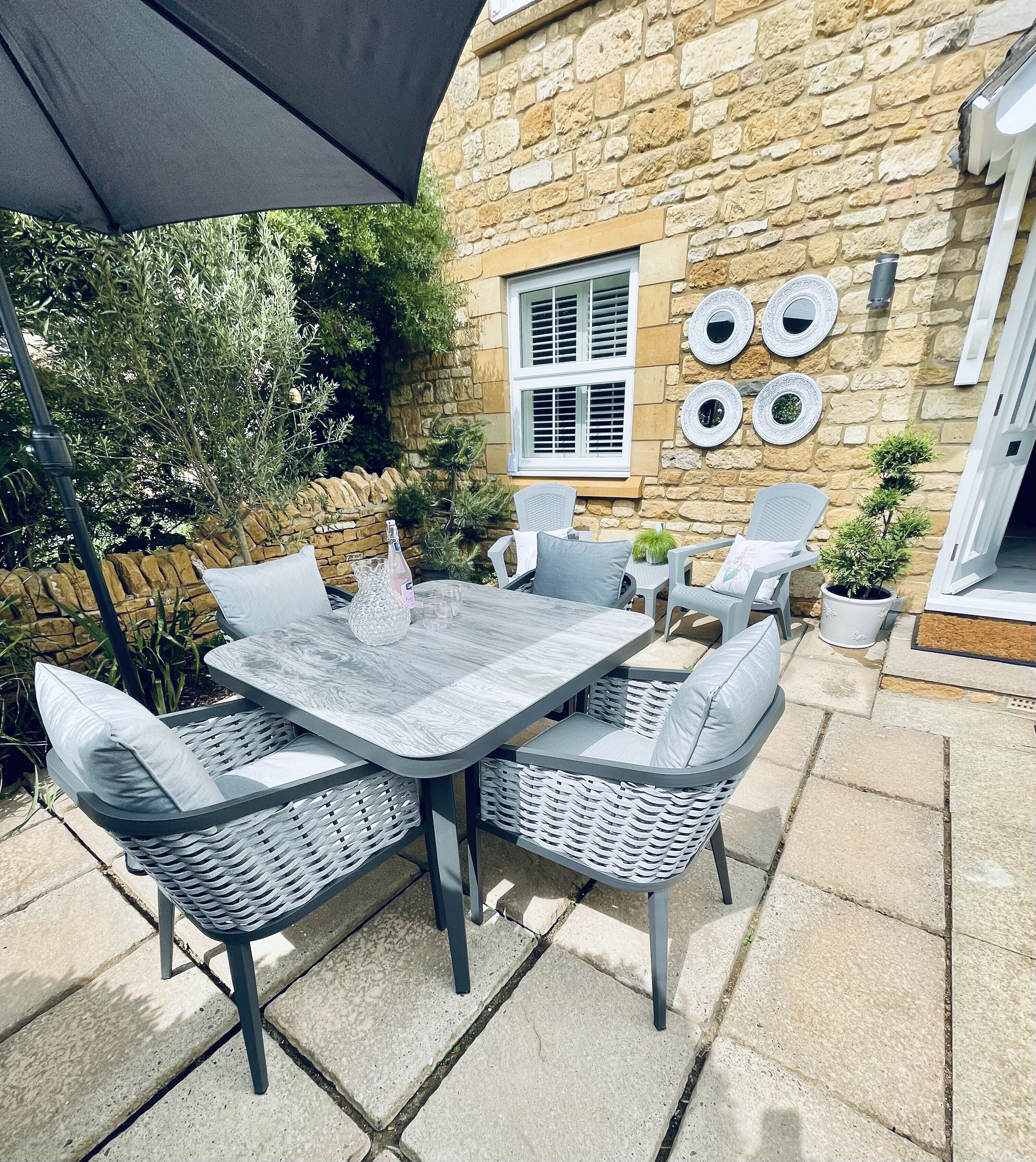 Een terras buiten, met een stenen muur, een tafel met stoelen en decoratieve borden aan de muur.