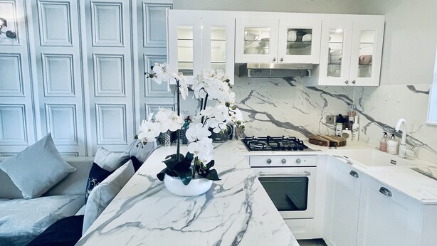 Una cocina moderna con armarios blancos, encimera de mármol y una isla central adornada con orquídeas blancas.